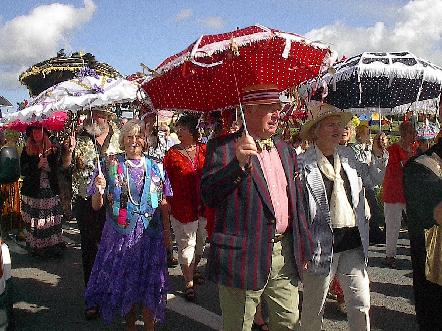 A parade with people in colourful outfits and hats holding decorated umbrellas