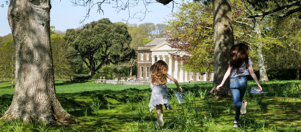 Two girls running barefoot through a field towards a grand house