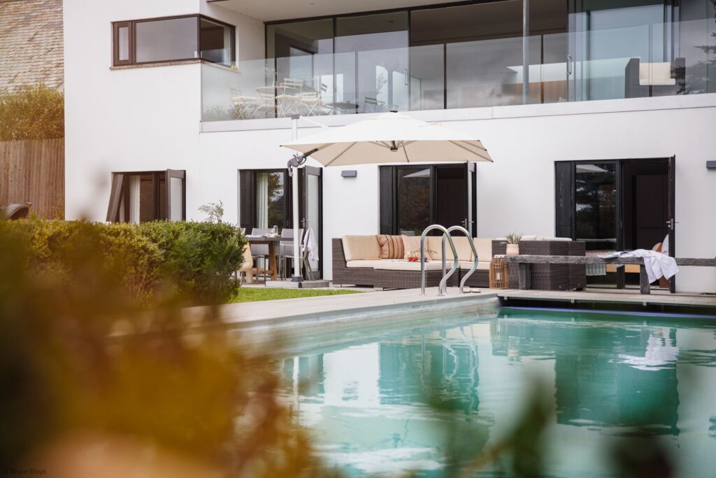 Modern white house with large windows, featuring a patio with a pool.