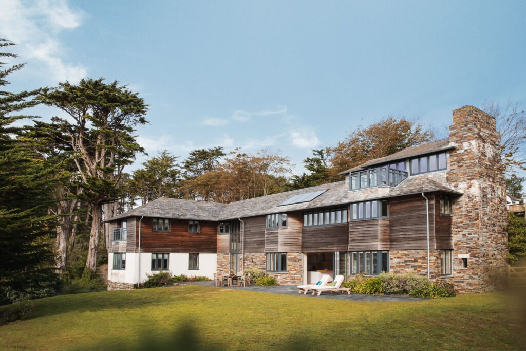 Modern house with stone and wood façade, large windows, and a chimney.