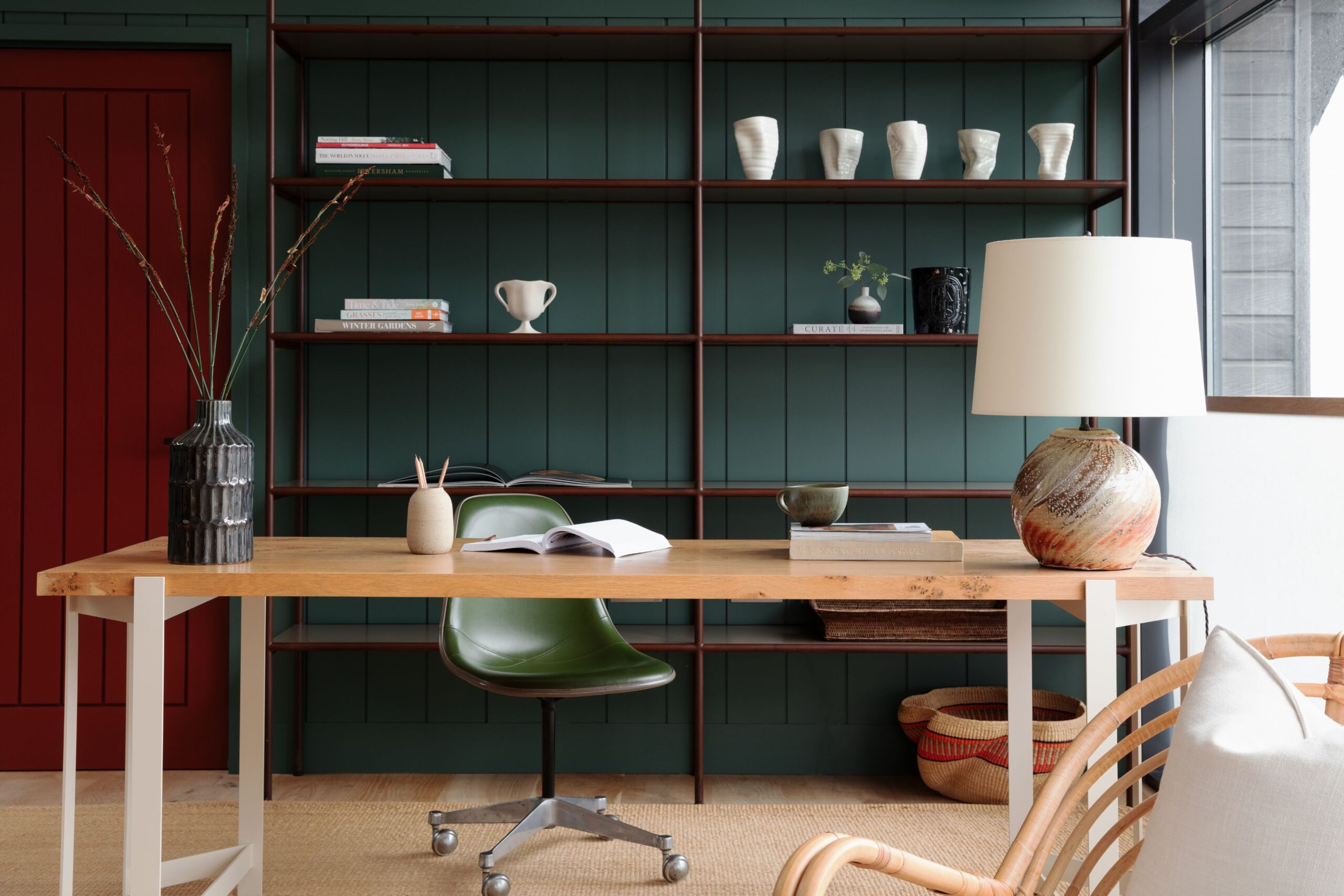 A modern home office with a wooden desk with a green chair, lamp, and open book.