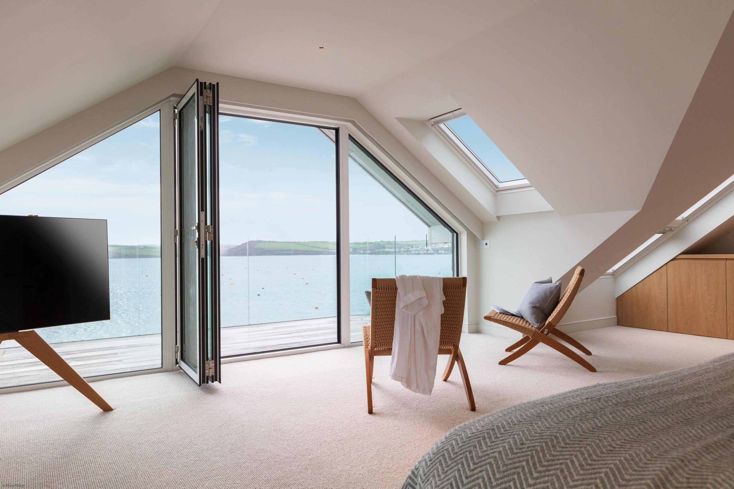 Bright room with slanted ceiling and open glass doors leading to a balcony overlooking water.