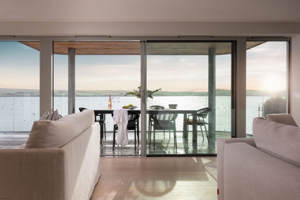 Modern living room with large glass doors opening to a waterfront view.