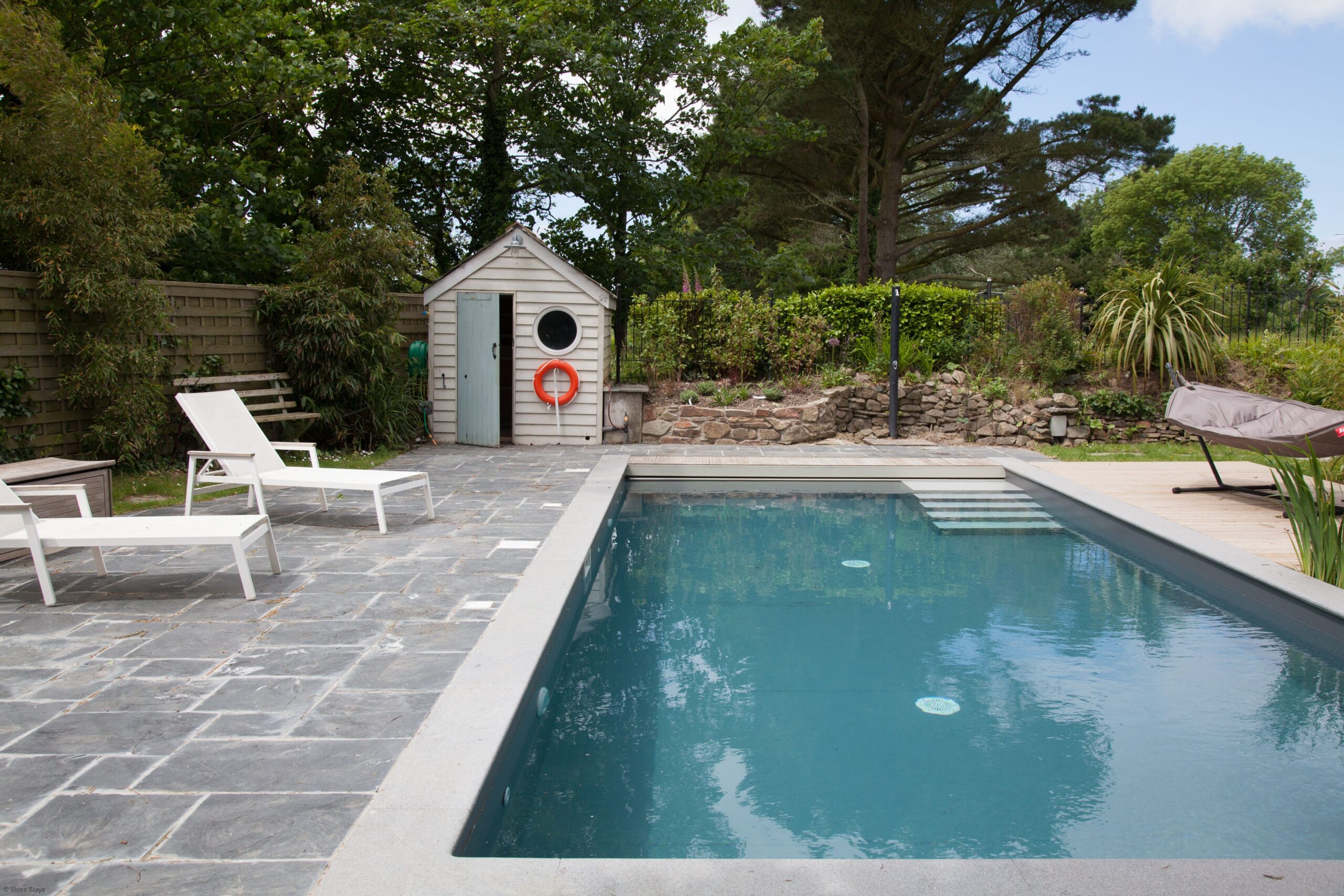 A rectangular pool with clear blue water, surrounded by grey stone tiles.