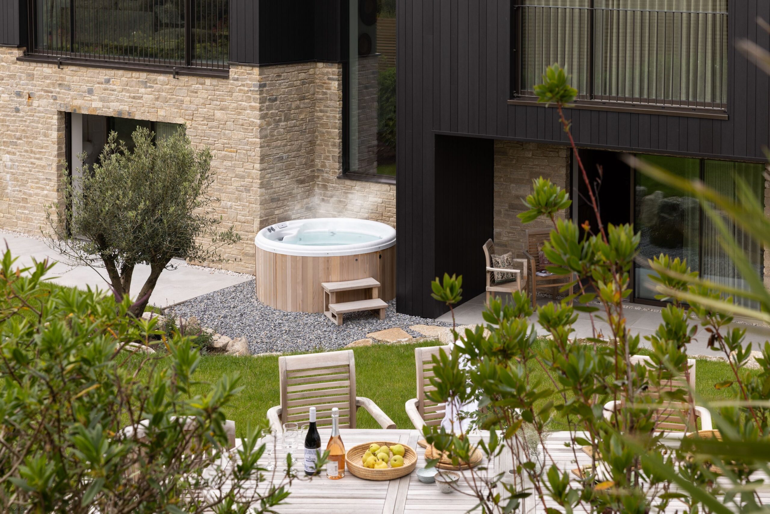 A steaming hot tub beside a stone and dark wood house.