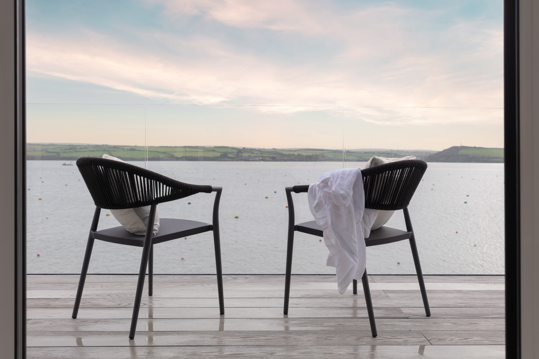 Two black chairs on a wooden deck overlooking an estuary