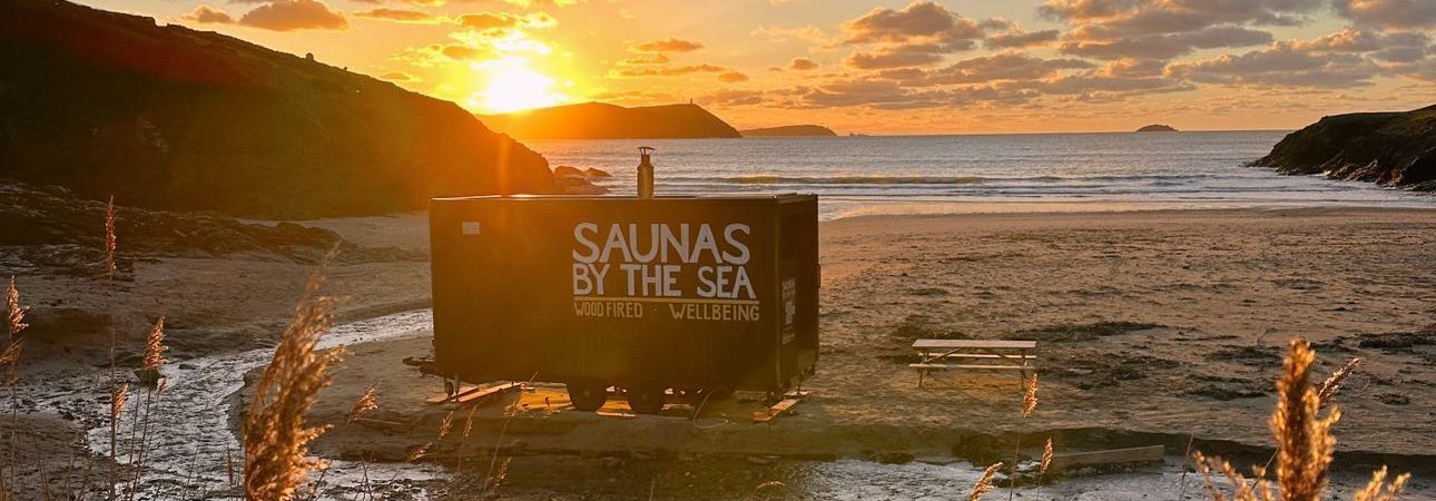 A beach at sunset with a "Saunas by the Sea" trailer on the sand