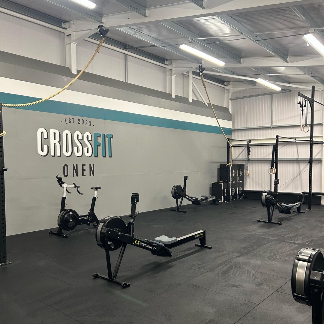 A gym interior with rowing machines, ropes, rings, and stacked boxes.