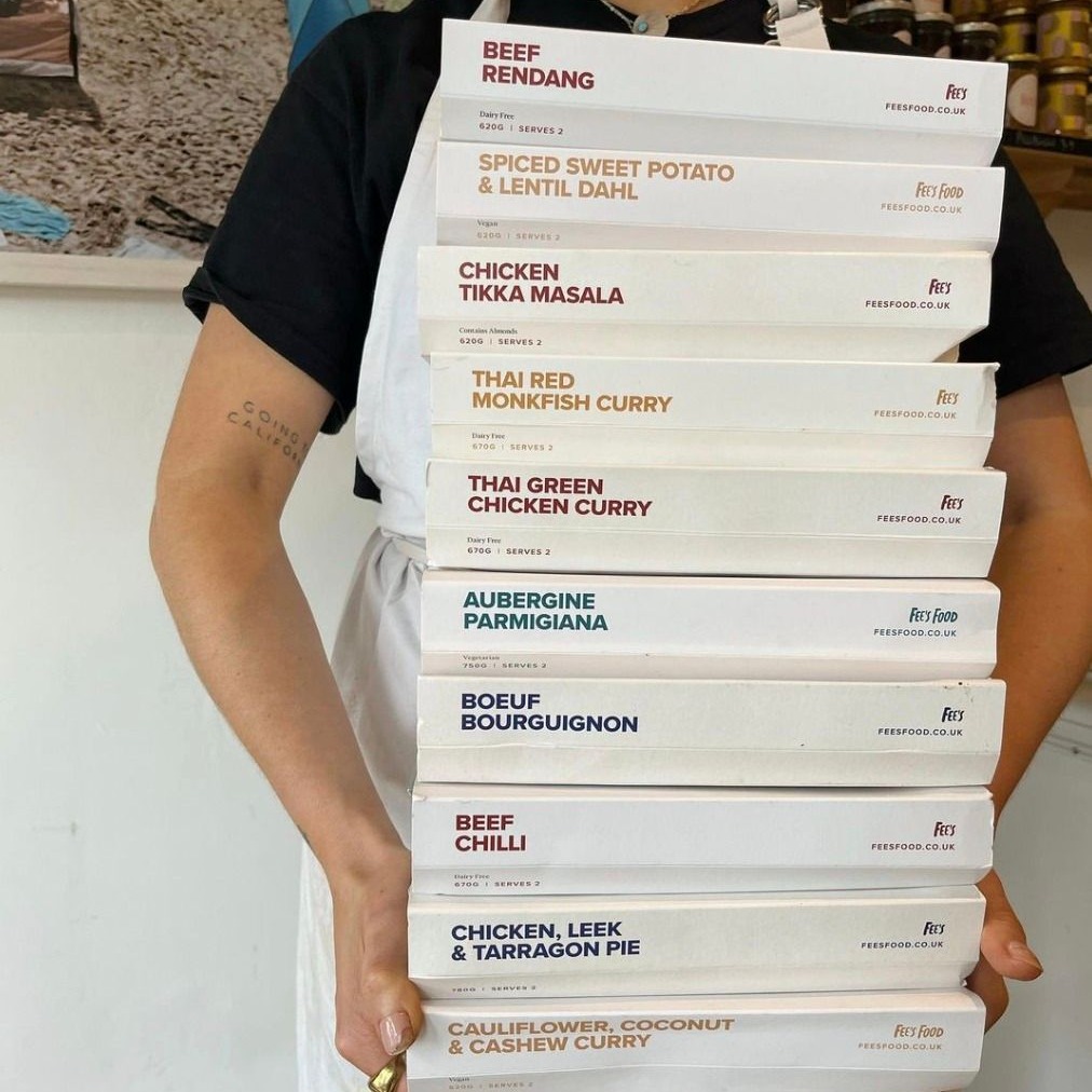 A person in an apron holding a stack of boxed meals.