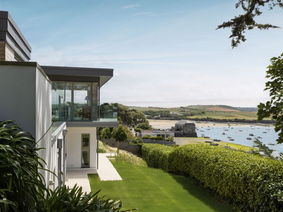 Modern house with large glass windows overlooking a garden and river filled with boats.