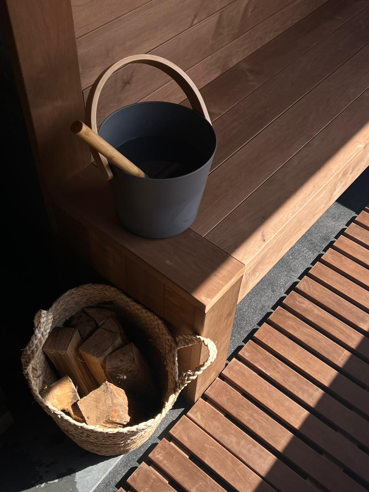 Wooden sauna bench with sunlight highlighting a bucket and ladle