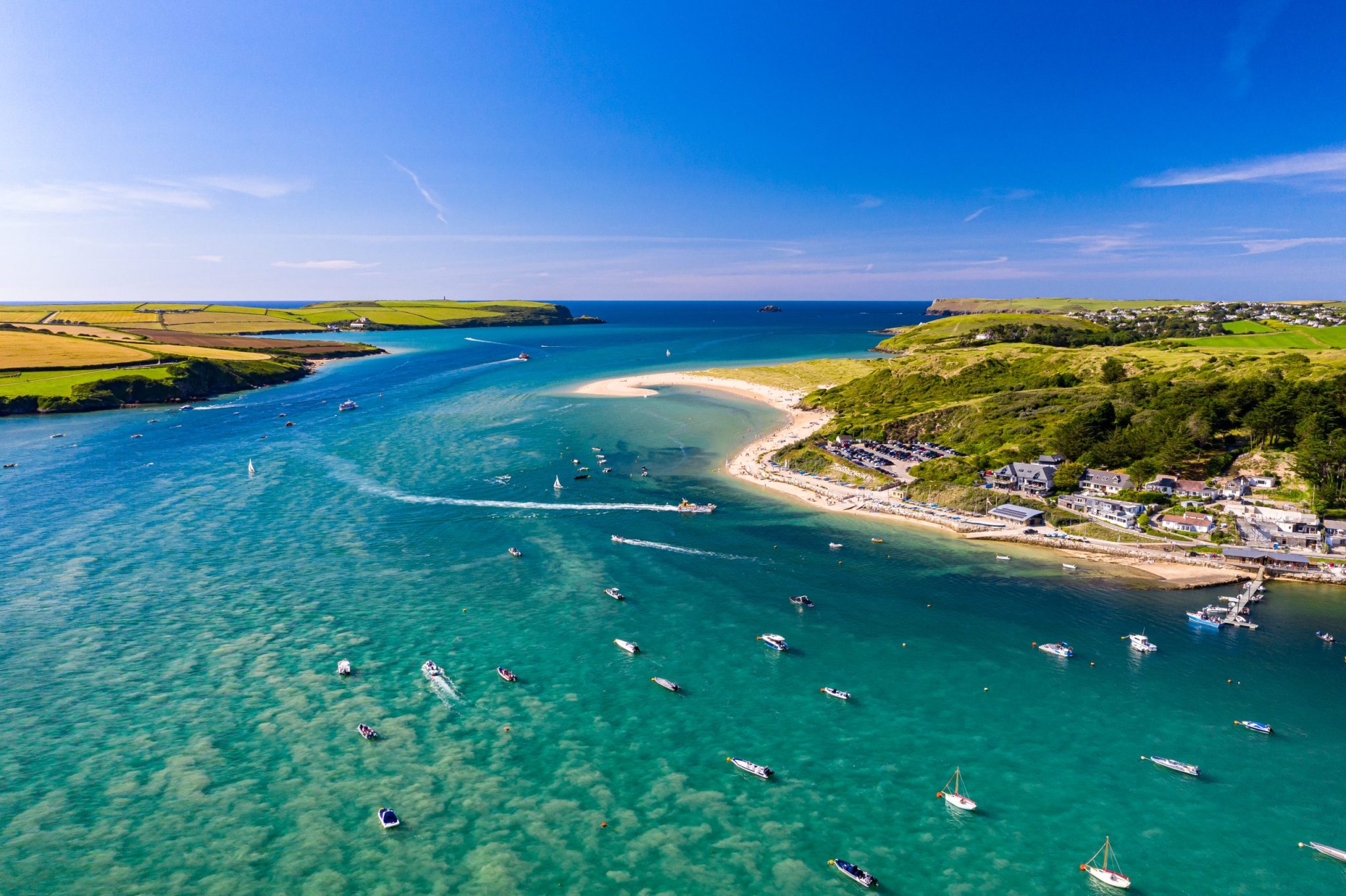 Aerial view of an estuary with boats scattered on the water near a sandy beach.