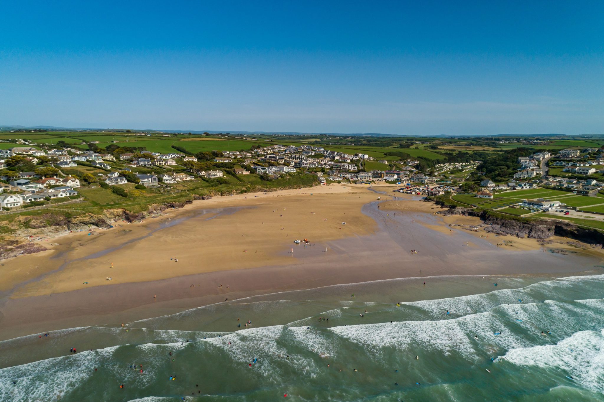 A sunny beach viewed from above, with waves coming in.