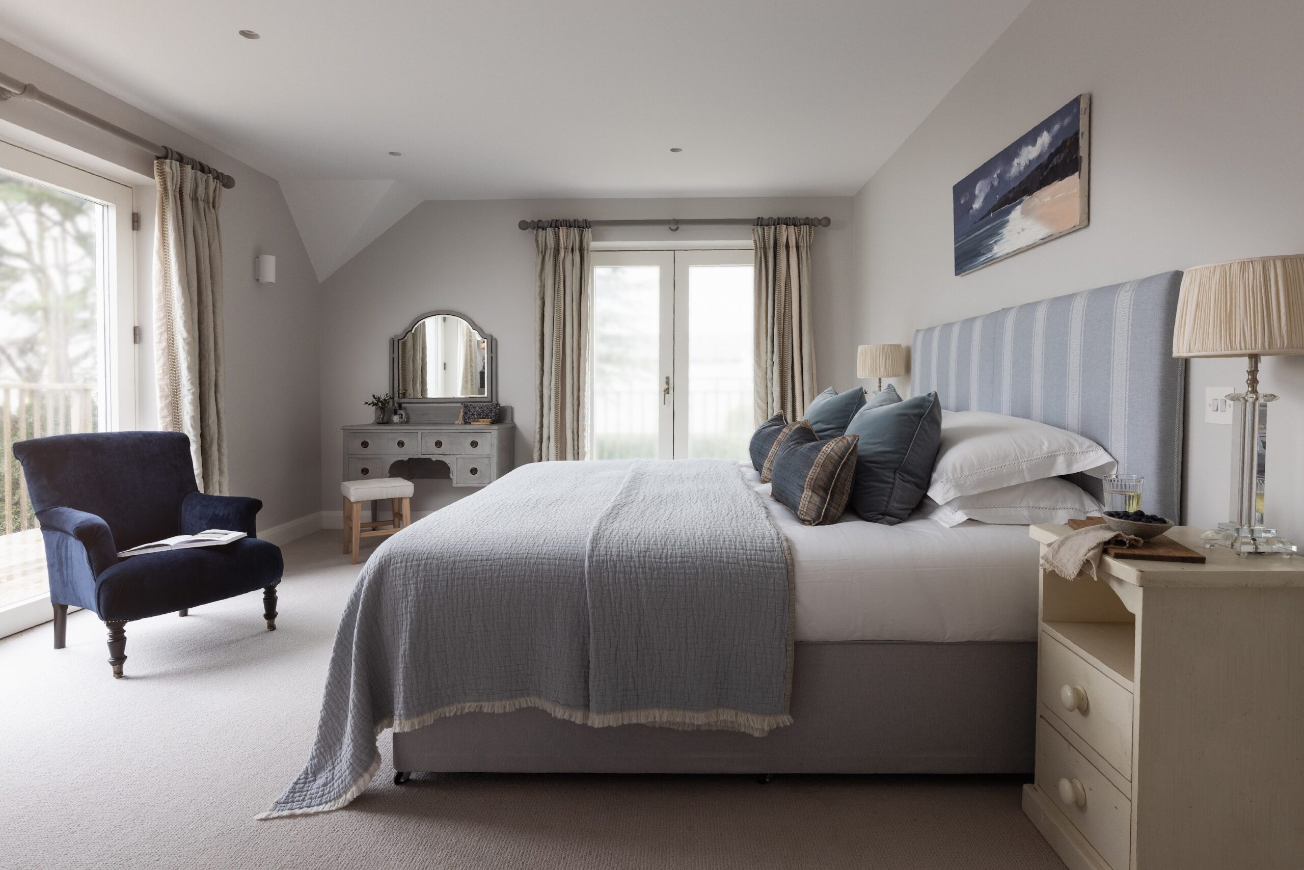 A bedroom with a large bed with blue and grey linens, flanked by bedside tables with lamps.