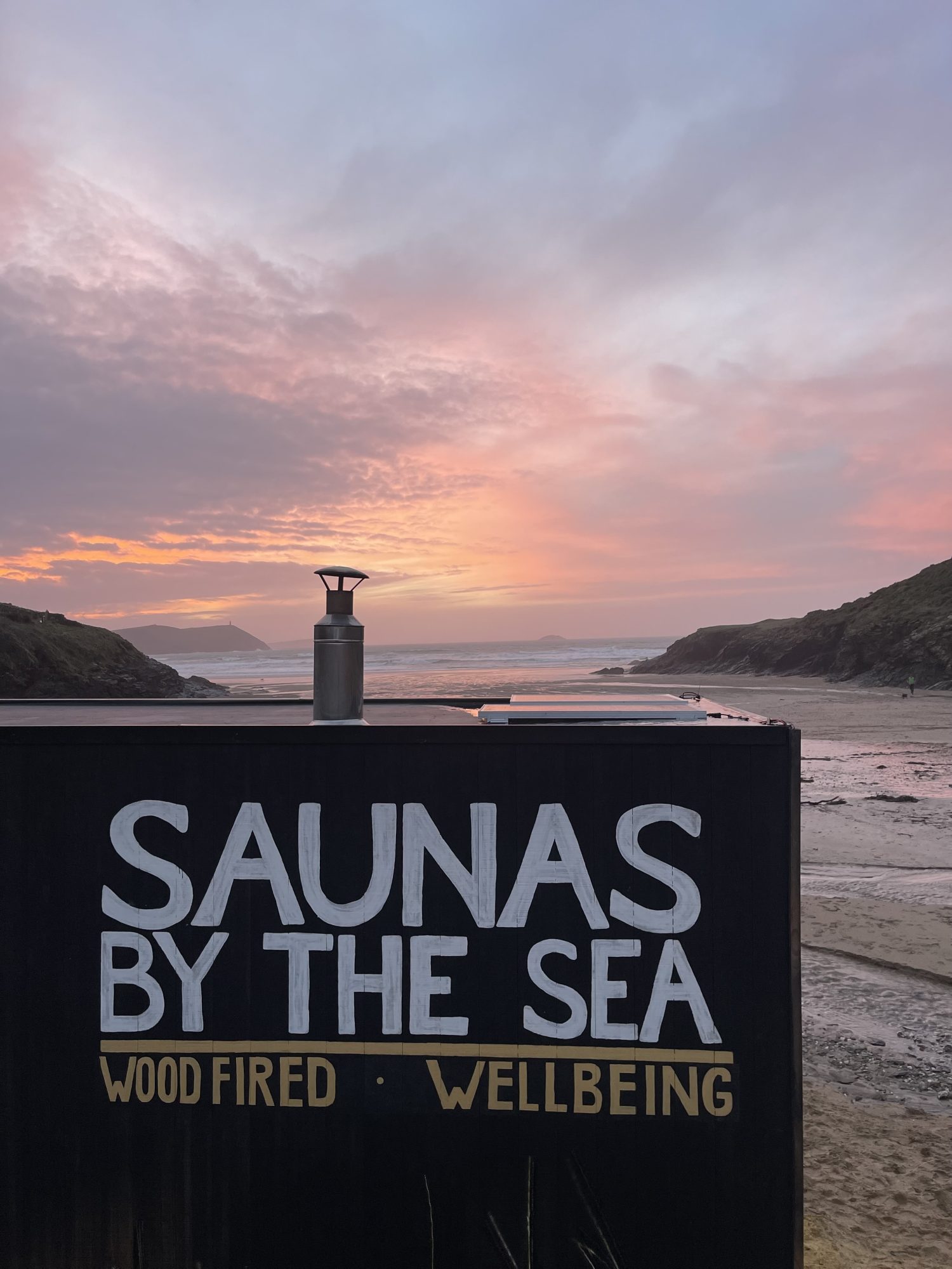 Sunset by the sea with a "Saunas by the Sea" sign in the foreground