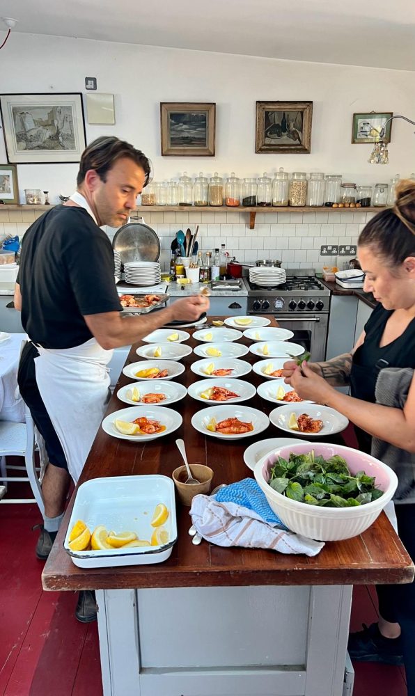 Two chefs in a kitchen plating dishes on a wooden table