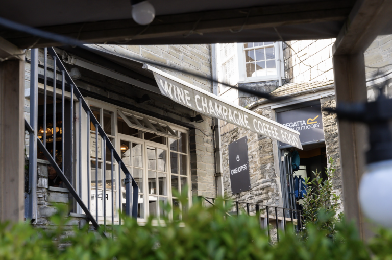 Café exterior with a mix of stone and windows, featuring a canopy sign reading "Wine Champagne Coffee Food."