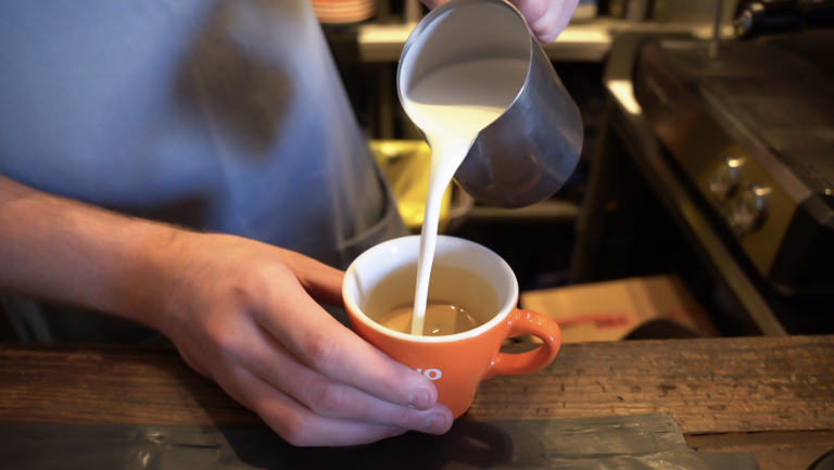 A person pouring milk into a cup of coffee in an orange mug