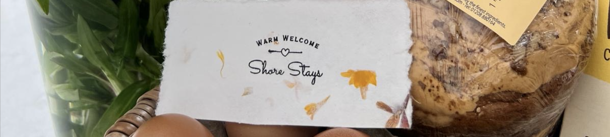 A card reading "Warm Welcome Shore Stays" on a tray with eggs, greens and a loaf of bread