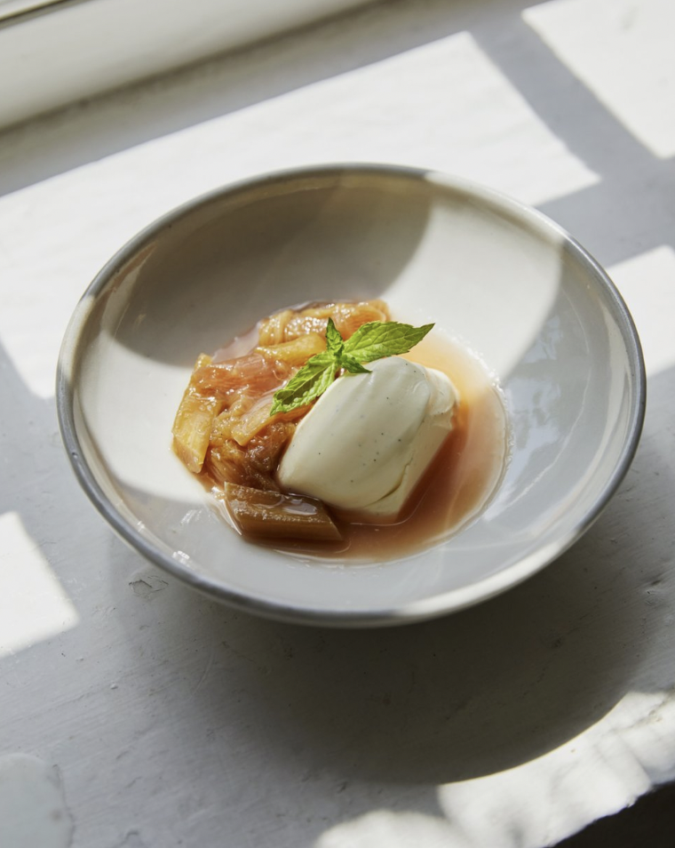 A ceramic bowl with a dessert with poached fruit, cream and a mint sprig