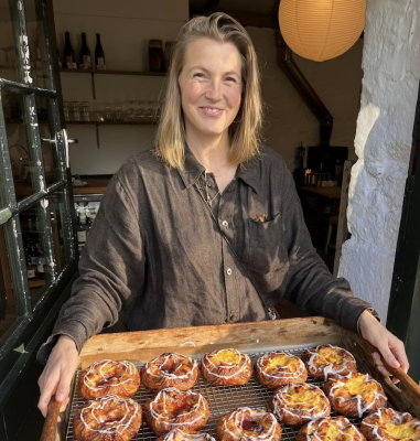 A woman smiling holding a tray of freshly baked pastries with icing