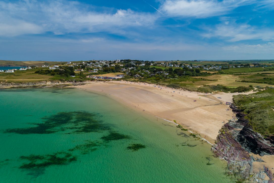 Aerial view of a beach with turquoise waters and golden sand, bordered by cliffs.
