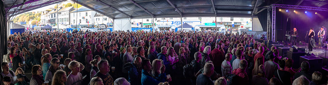 Panoramic view of a crowded indoor music festival with an audience facing a stage