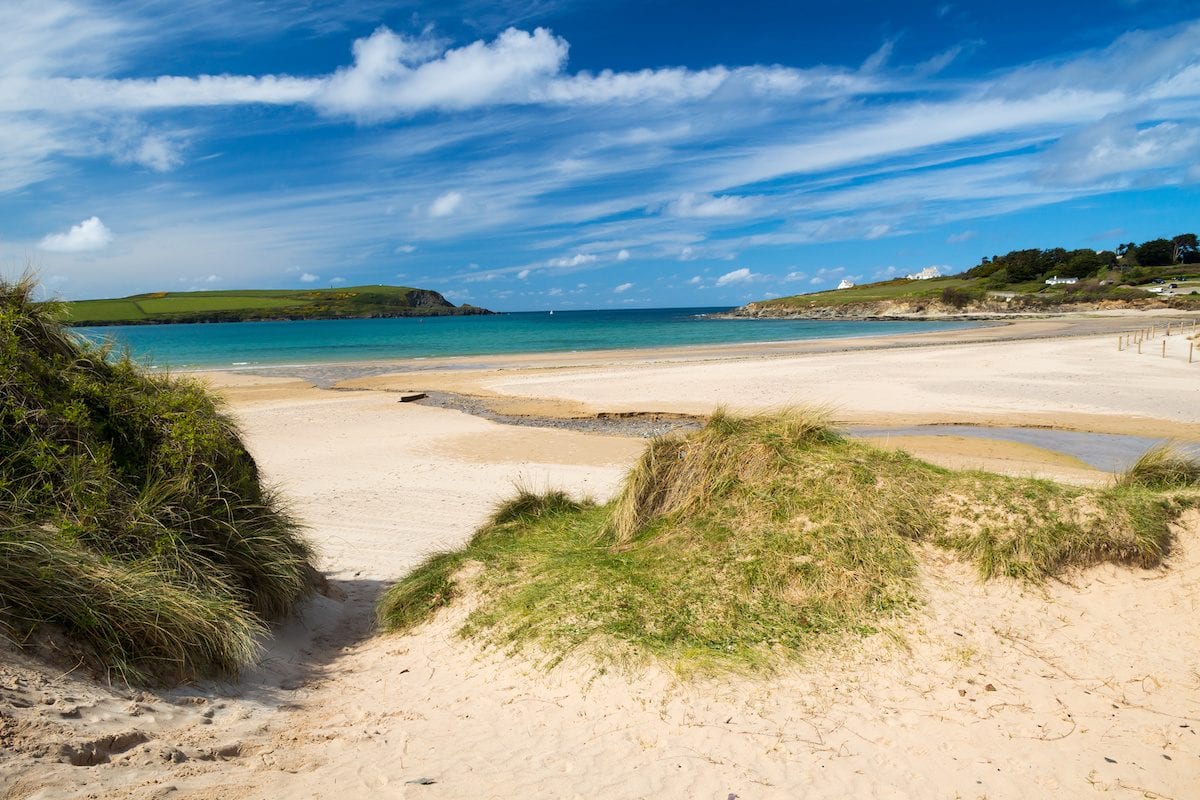 A beach with a blue sea under a bright sky with scattered clouds.